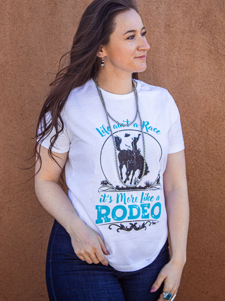 A woman wearing a white t-shirt with the text 'Life's Not a Race, it's more like a Rodeo' and an illustration of a bucking bronco in turquoise and black inks.