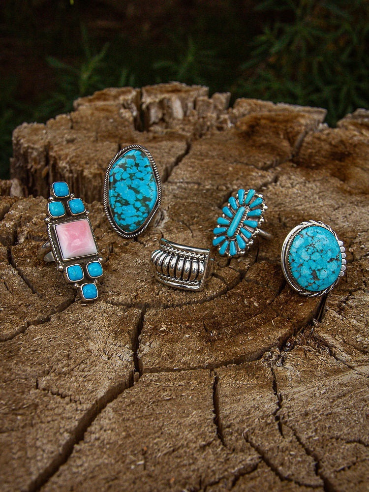 Five turquoise and silver rings on a wooden surface